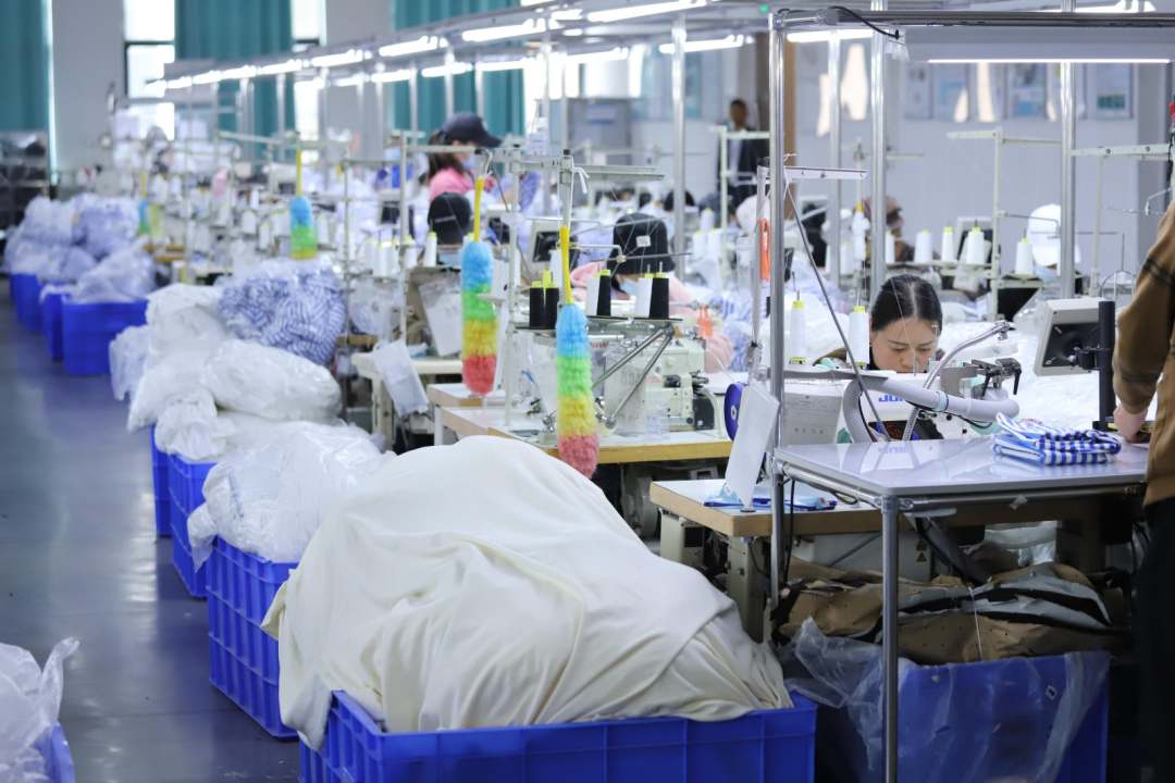 圖為工廠內(nèi)工人縫制衣物,一派繁忙景象。