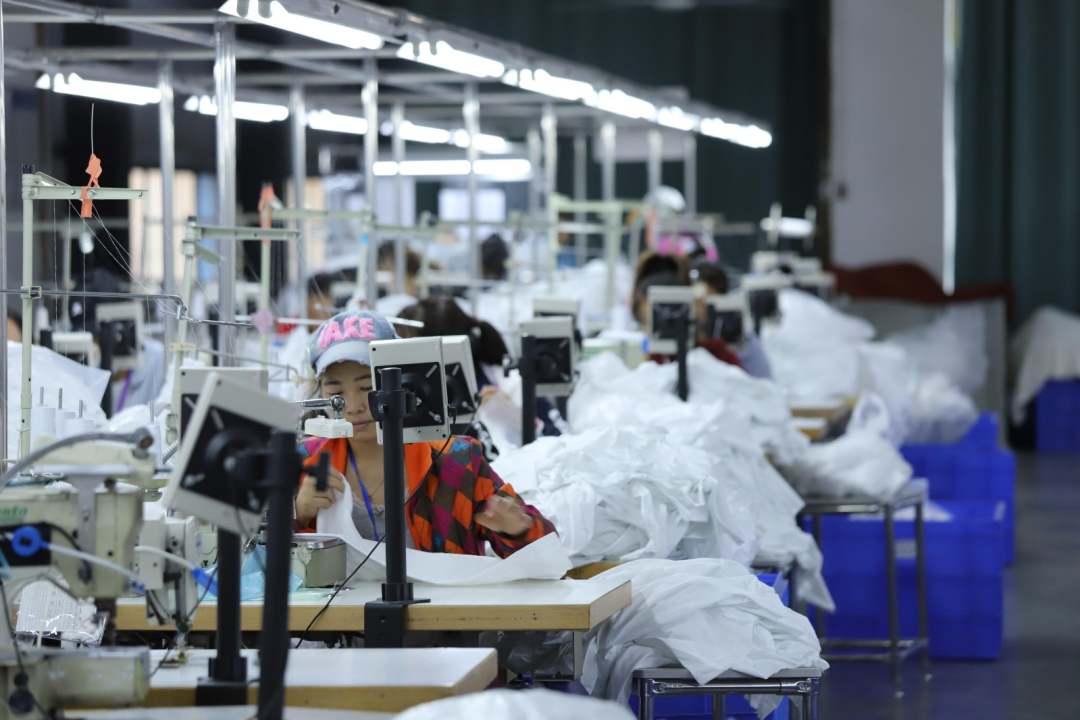 圖為工廠內(nèi)工人縫制衣物,一派繁忙景象。