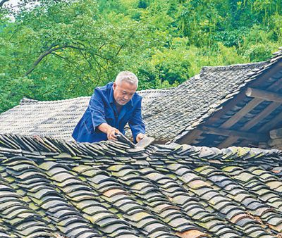 圖為萬明春在撿瓦，修補(bǔ)漏雨的地方。蘇 濱 涂 敏攝影報道